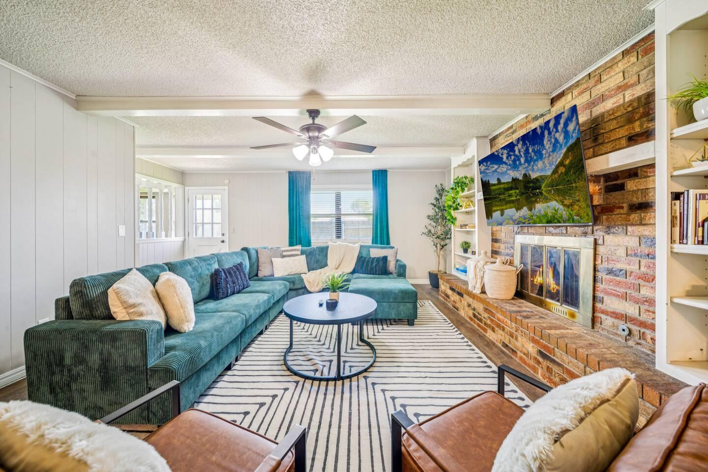Living Room – Includes a large sectional sofa, wall-mounted TV and brick fireplace.