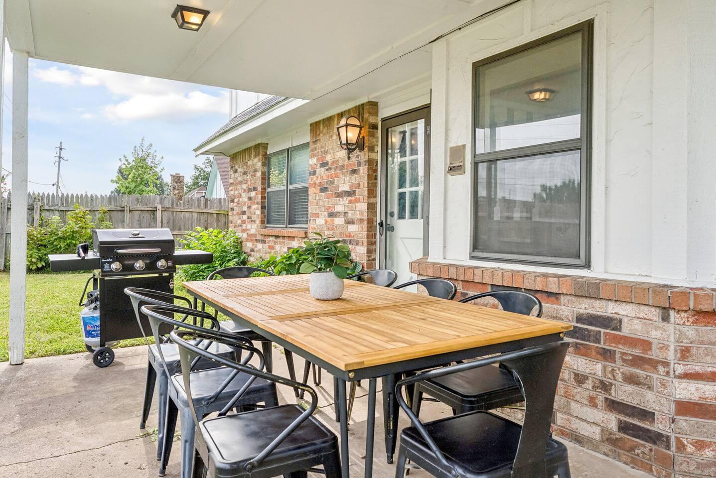 Patio – Covered outdoor space with a dining table for six, gas grill, overhead lighting, and access to a fenced backyard.