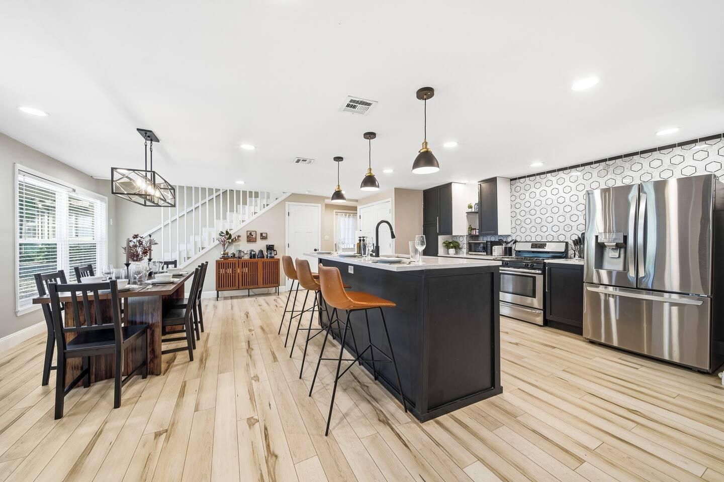 Kitchen – Modern kitchen with stainless steel appliances, dark cabinets, and a large island with bar seating. Features pendant lighting, light wood floors, and a hexagon tile backsplash.