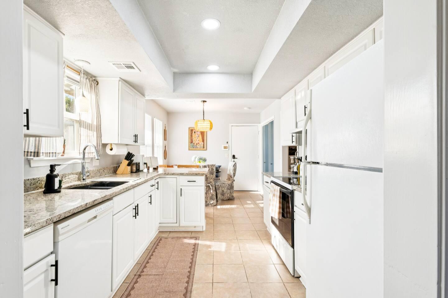 Kitchen: A bright kitchen with white cabinets, granite countertops, and stainless steel appliances. A dining area with a hanging light fixture is visible at the far end.