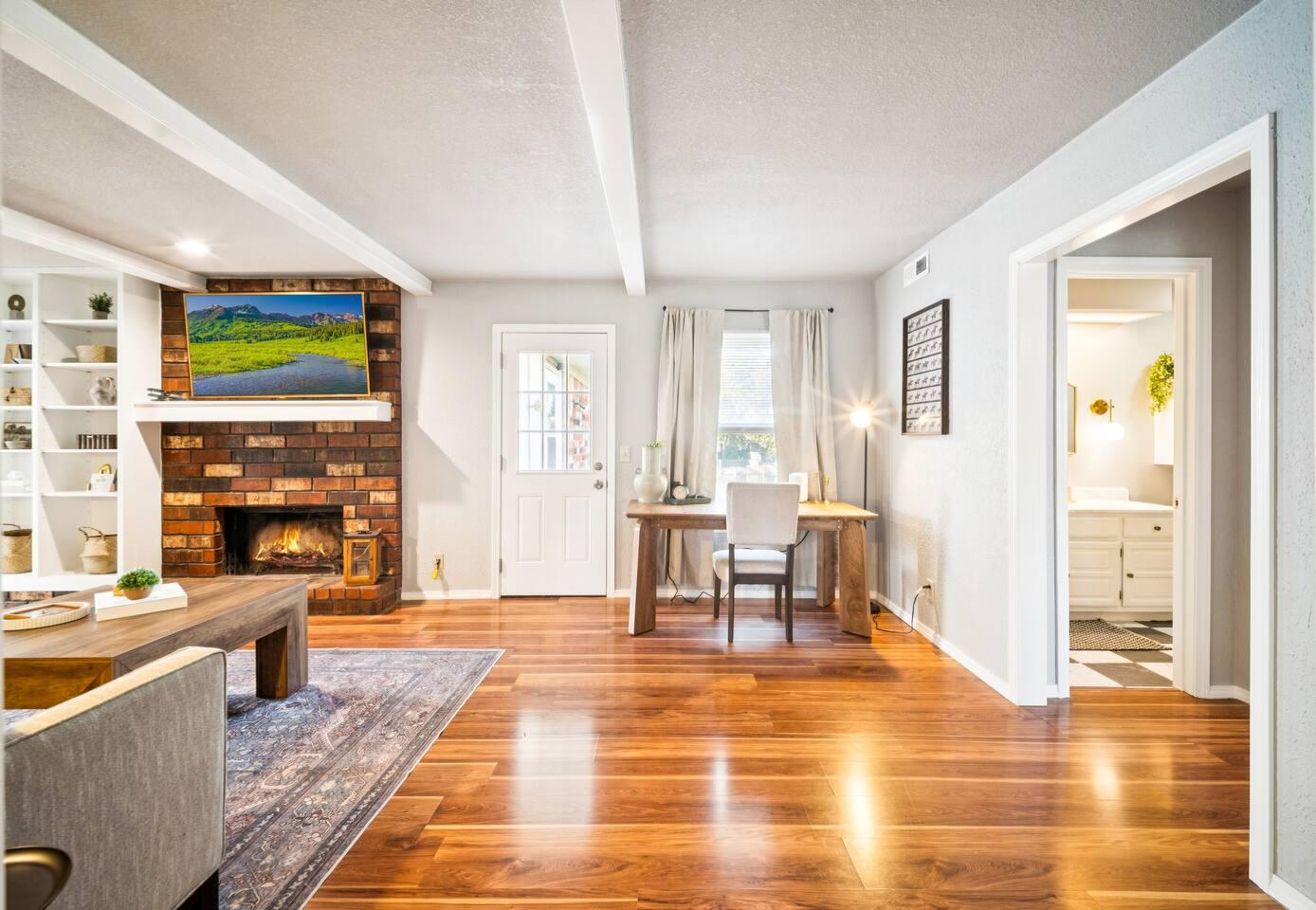 Living Room: A view of the living room showing a brick fireplace with a TV mounted above, a wooden desk with a chair beside the door, and an open doorway leading to the bathroom.