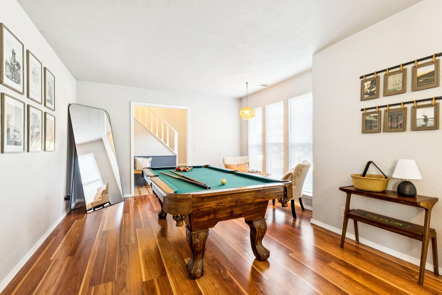 Living room – A room with a pool table, hardwood floors, framed artwork on the walls, large windows, and a full-length mirror.