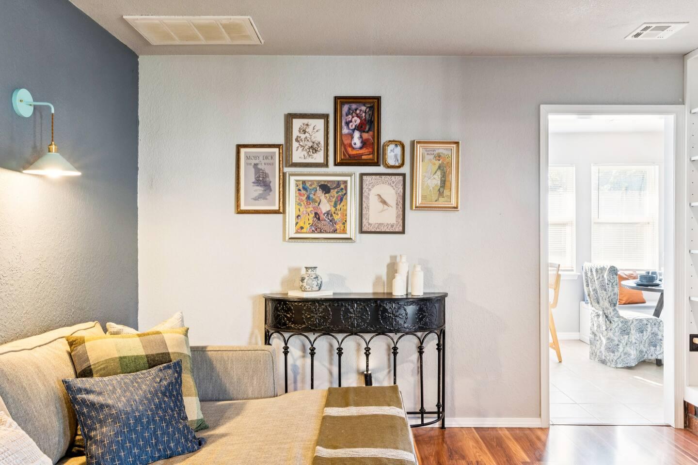 Living Room: A side view of the living room showing part of the sectional sofa, a decorative console table with vases, and a gallery wall with framed art pieces.